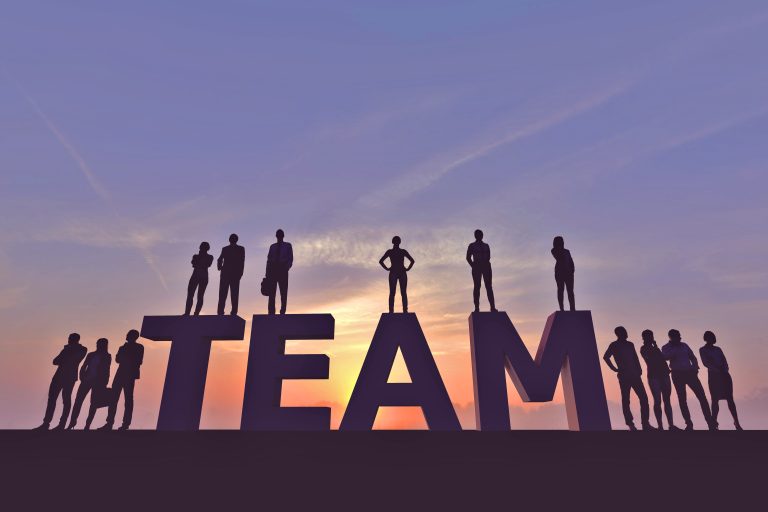 商业团队的剪影站在夕阳下的“team”字样上，象征着合作与成功。